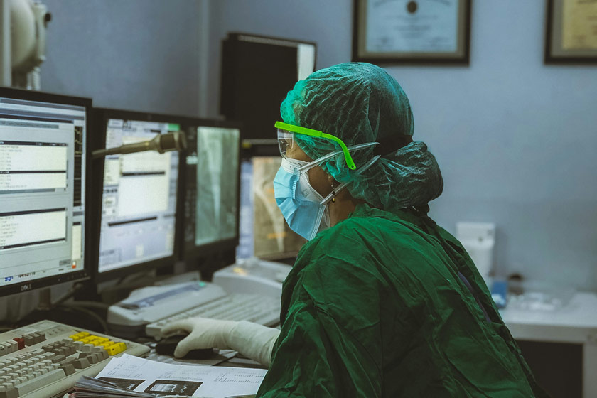 medical professional wearing protective scrubs mask and gloves reading charts on computer